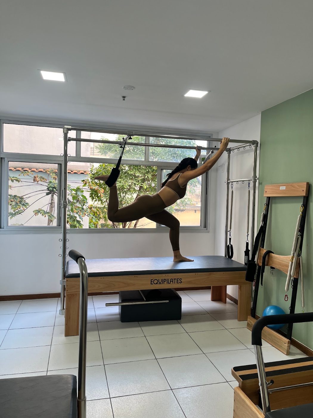 Aluna em exercício no Cadillac, sala com janelas amplas